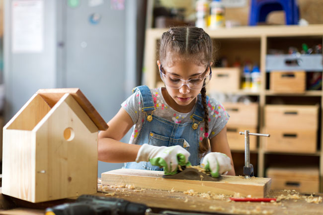 Un enfant bricole sa maison en bois en ayant des protections